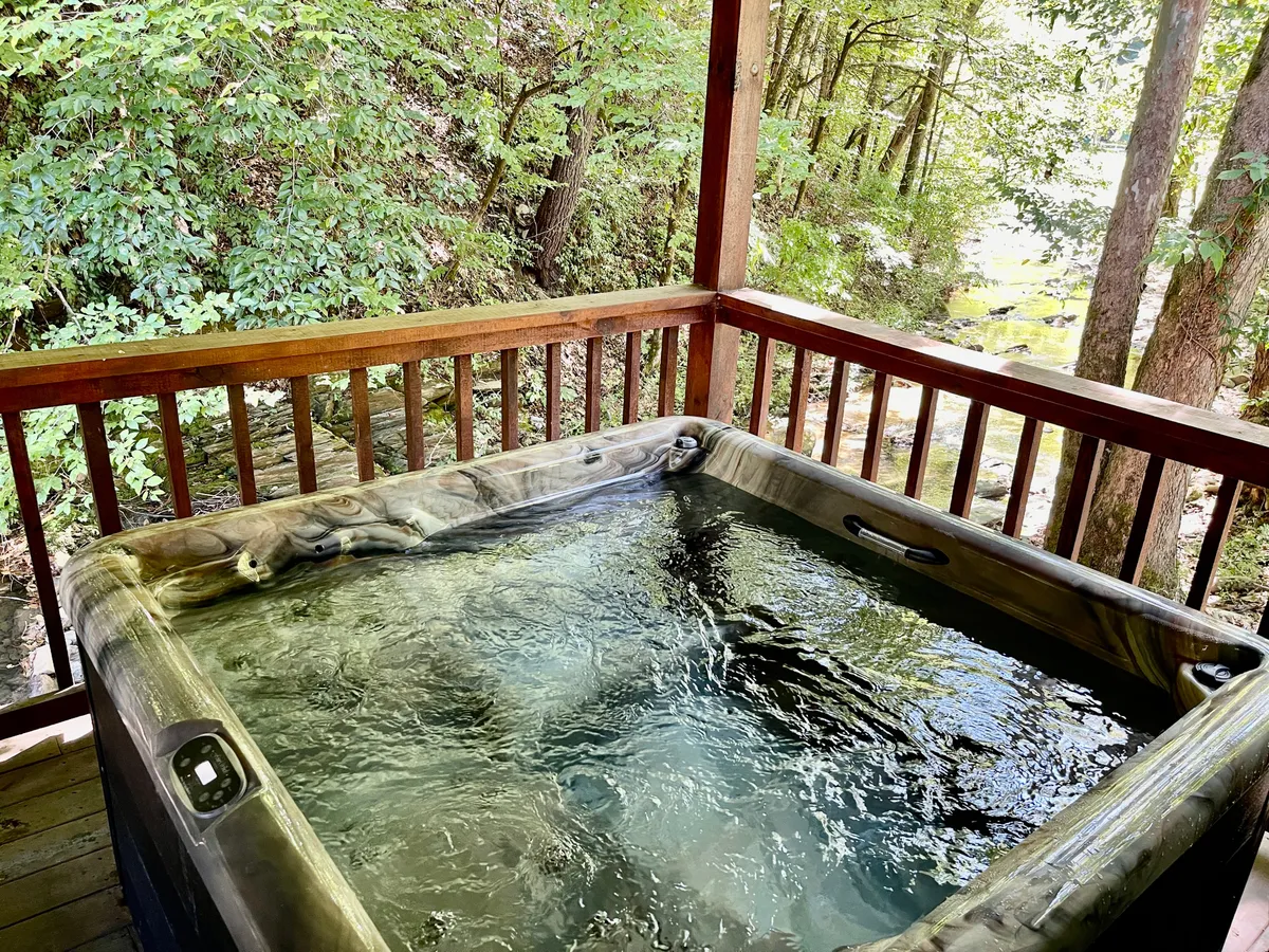 This serene exterior shot features the cabin's hot tub set against a backdrop of greenery and natural wood. The image evokes the relaxation families can enjoy after a day of adventure, highlighting the hot tub as a gathering spot for stargazing and creating cherished memories.