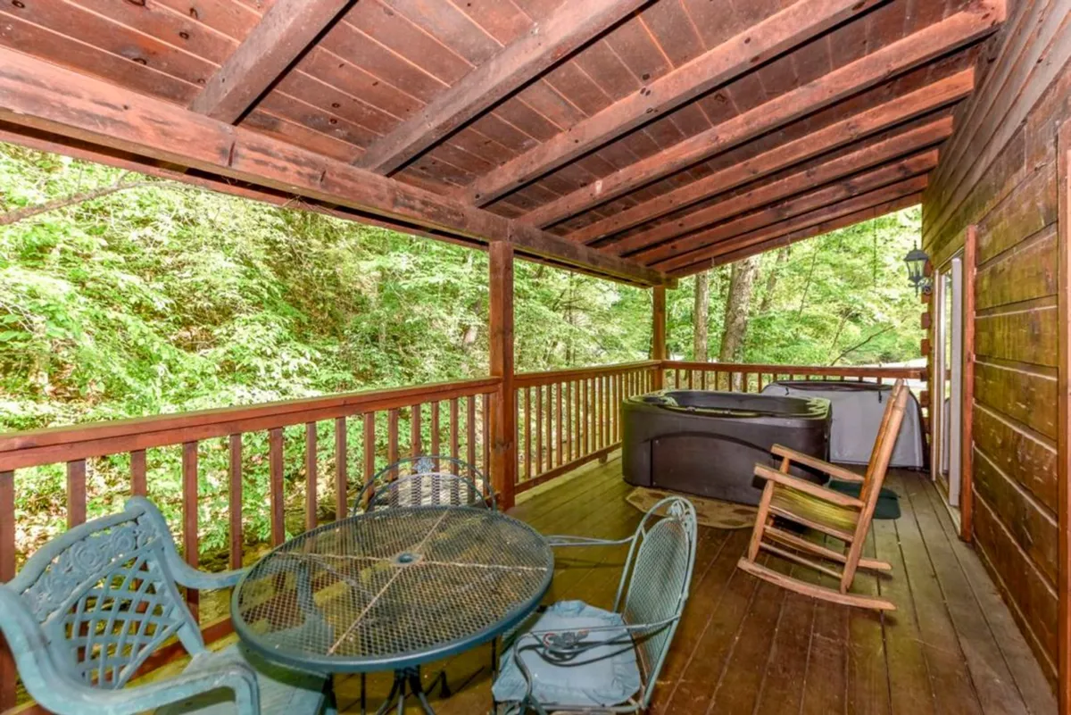 This image presents a tranquil outdoor seating area adjoining a wooden deck surrounded by lush greenery. The focal points include a hot tub nestled within the deck, comfortable seating for groups, and a backdrop of natural woodland, emphasizing relaxation and immersion in nature.