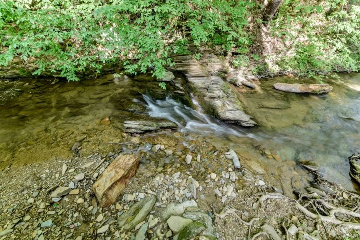 This image showcases a tranquil outdoor scene featuring a gently flowing stream bordered by smooth rock formations and lush, green foliage. The surrounding landscape offers inviting spots for nature walks and peaceful moments by the water, all framed by the serenity and beauty of the Smoky Mountains.