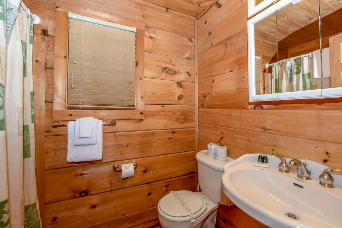 An inviting bathroom with natural wooden walls, a bright window, a sink, and a toilet. The design feels fresh, clean, and thoughtfully maintained, suggesting attention to guest comfort and detail.