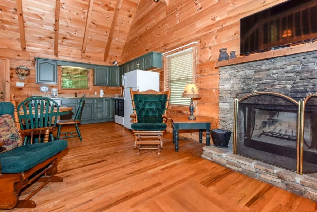A cozy, stylish interior with a fireplace as the centerpiece, surrounded by comfortable green chairs and a dining table. The setting conveys warmth, relaxation, and communal activities like dining and socializing.