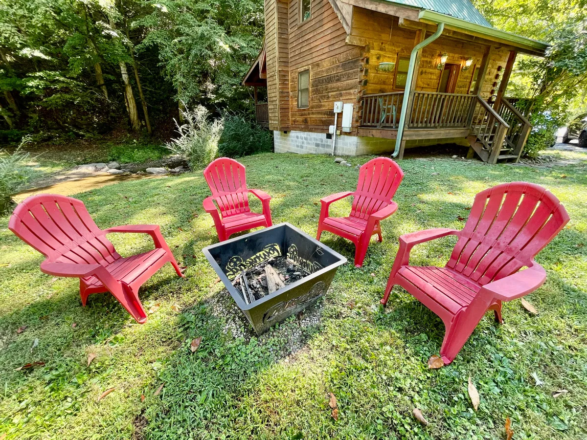 The photo features a cozy fire pit encircled by red Adirondack chairs, set against the backdrop of a rustic wooden cabin. The setup invites guests to gather, share stories, and enjoy s’mores under the open sky, creating a warm, inviting atmosphere for families and friends.
