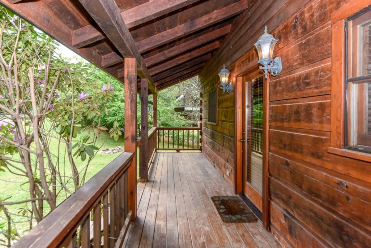 This image captures the welcoming exterior of Creekside Cabin, with its inviting wooden porch, warm lamps, and lush green surroundings. The scene highlights a space perfect for relaxing, greeting family members, or enjoying the fresh Smoky Mountain air together.