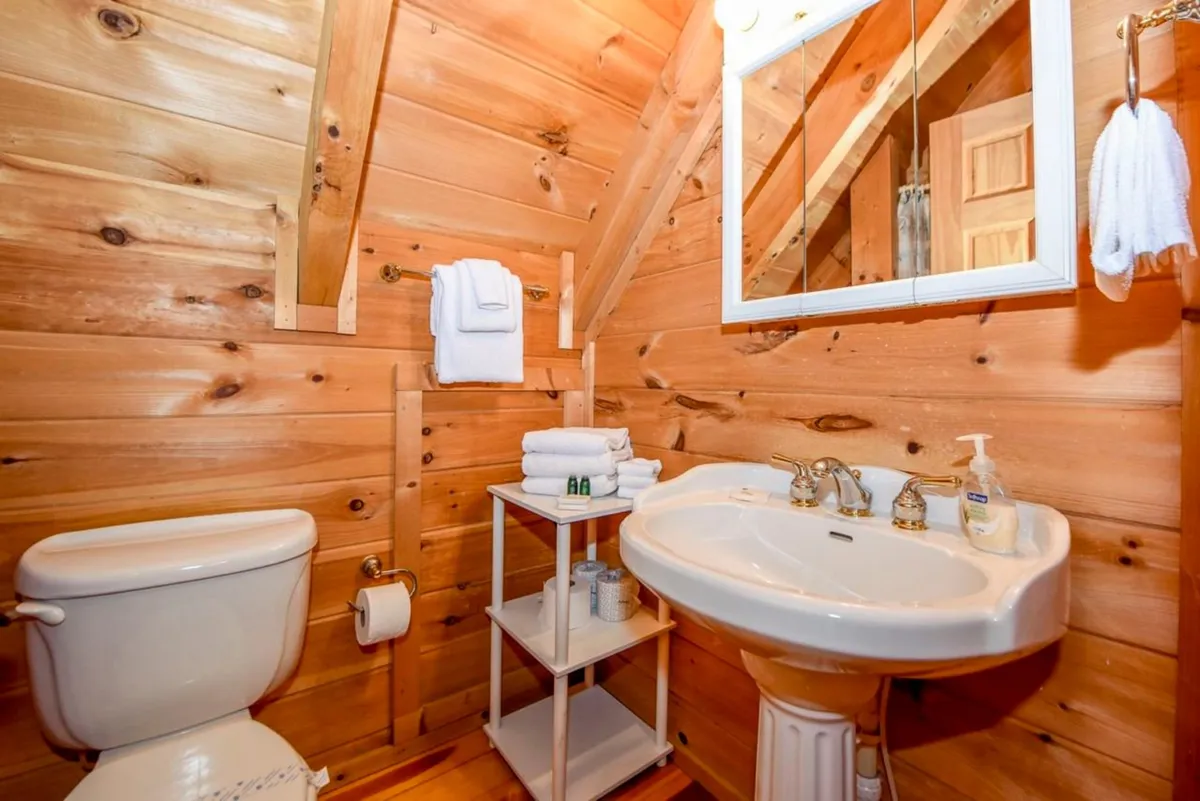 A warmly lit bathroom with wood-paneled walls, a vintage sink faucet, and neatly folded towels on a shelf. The thoughtful details create a soothing, spa-like feel, suggesting a space designed for relaxation and pampering.